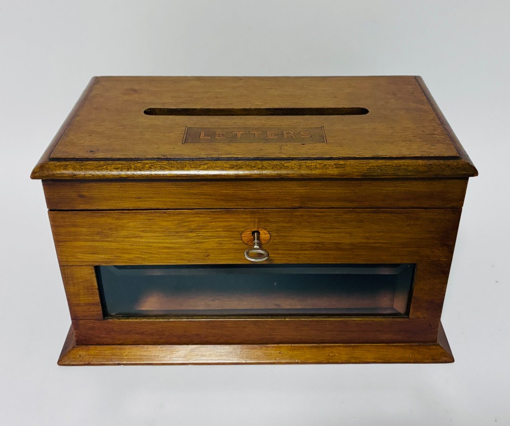 An antique mahogany tabletop letter box featuring a top posting slot, carved LETTERS plaque, key lock mechanism, and bevelled glass front panel.