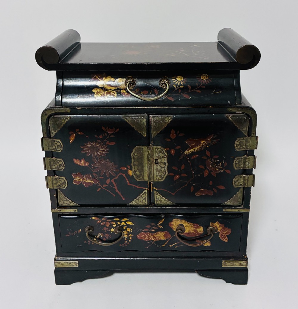 A black lacquered Japanese tabletop cabinet featuring hand-painted botanical motifs and decorative engraved brass corner mounts.
