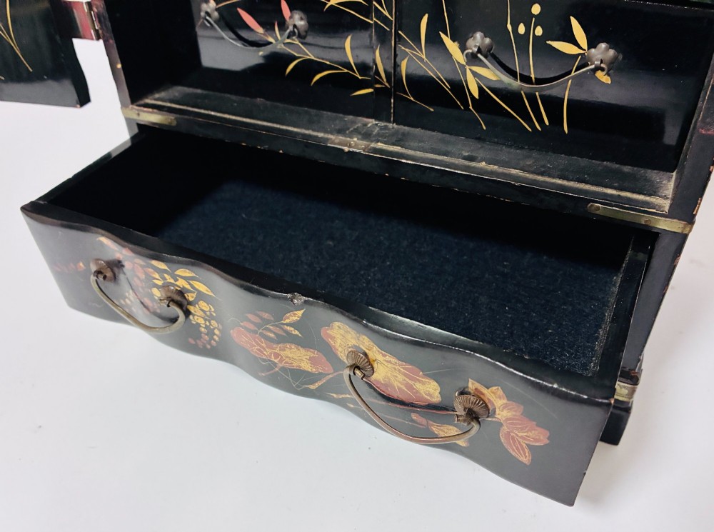 A black lacquered Japanese tabletop cabinet featuring hand-painted botanical motifs and decorative engraved brass corner mounts. View VIII