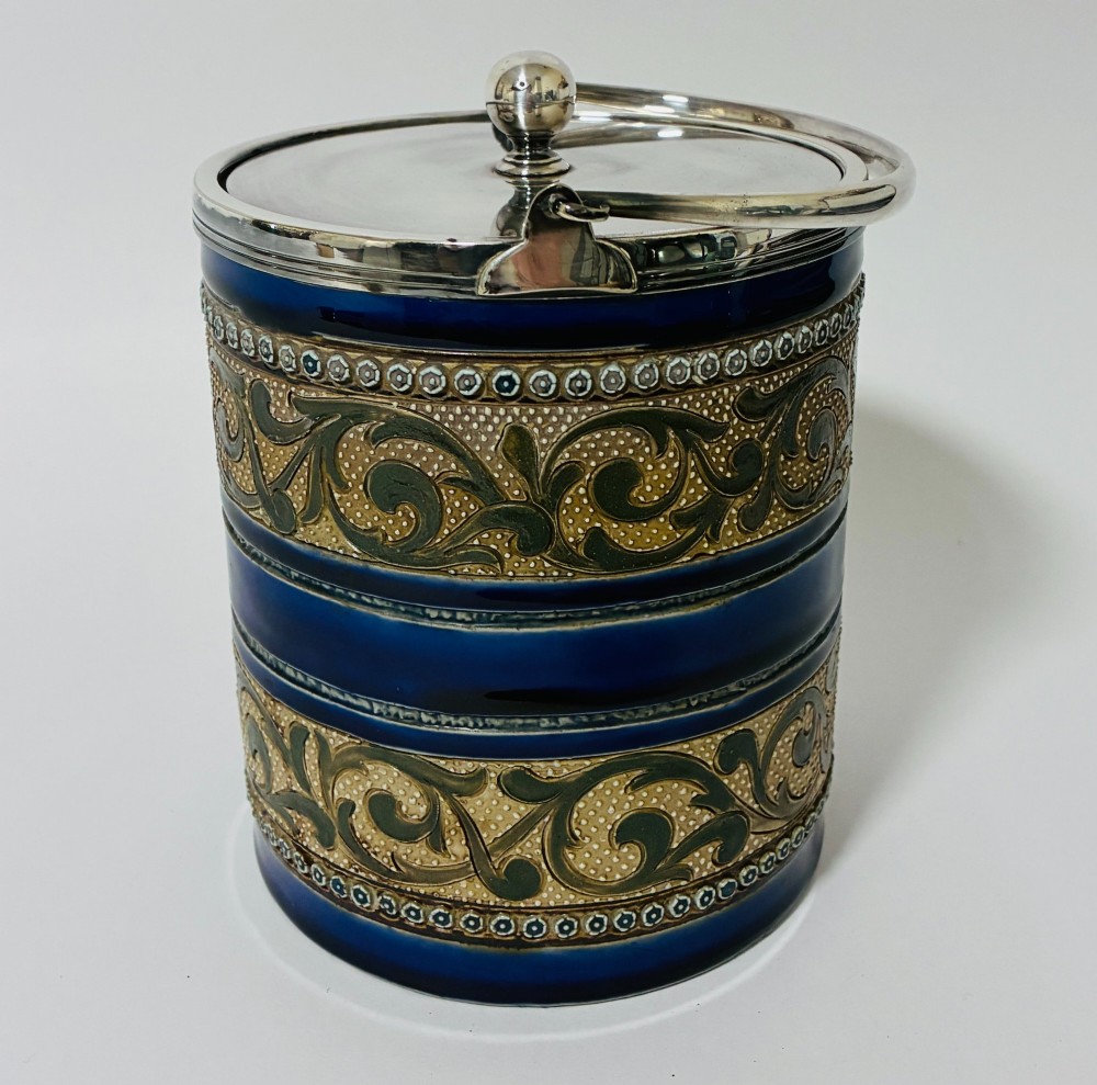 A cylindrical Victorian Doulton Lambeth stoneware biscuit barrel featuring cobalt blue and beige scrollwork decoration, fitted with a silver-plated lid, swing handle, and finial. View II
