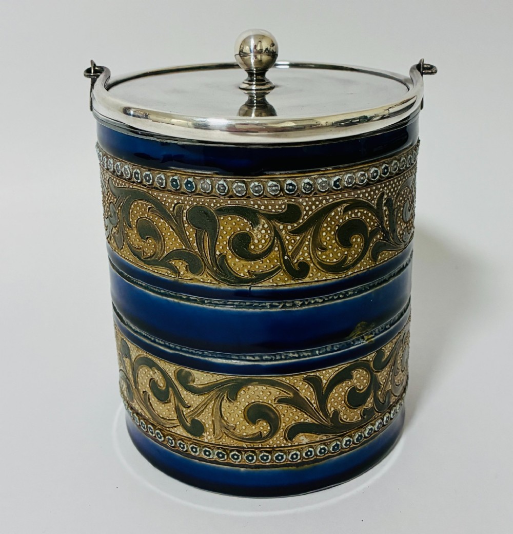 A cylindrical Victorian Doulton Lambeth stoneware biscuit barrel featuring cobalt blue and beige scrollwork decoration, fitted with a silver-plated lid, swing handle, and finial. View III