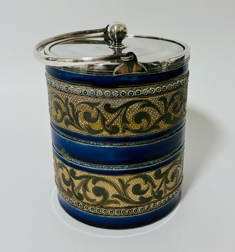 A cylindrical Victorian Doulton Lambeth stoneware biscuit barrel featuring cobalt blue and beige scrollwork decoration, fitted with a silver-plated lid, swing handle, and finial. View IV