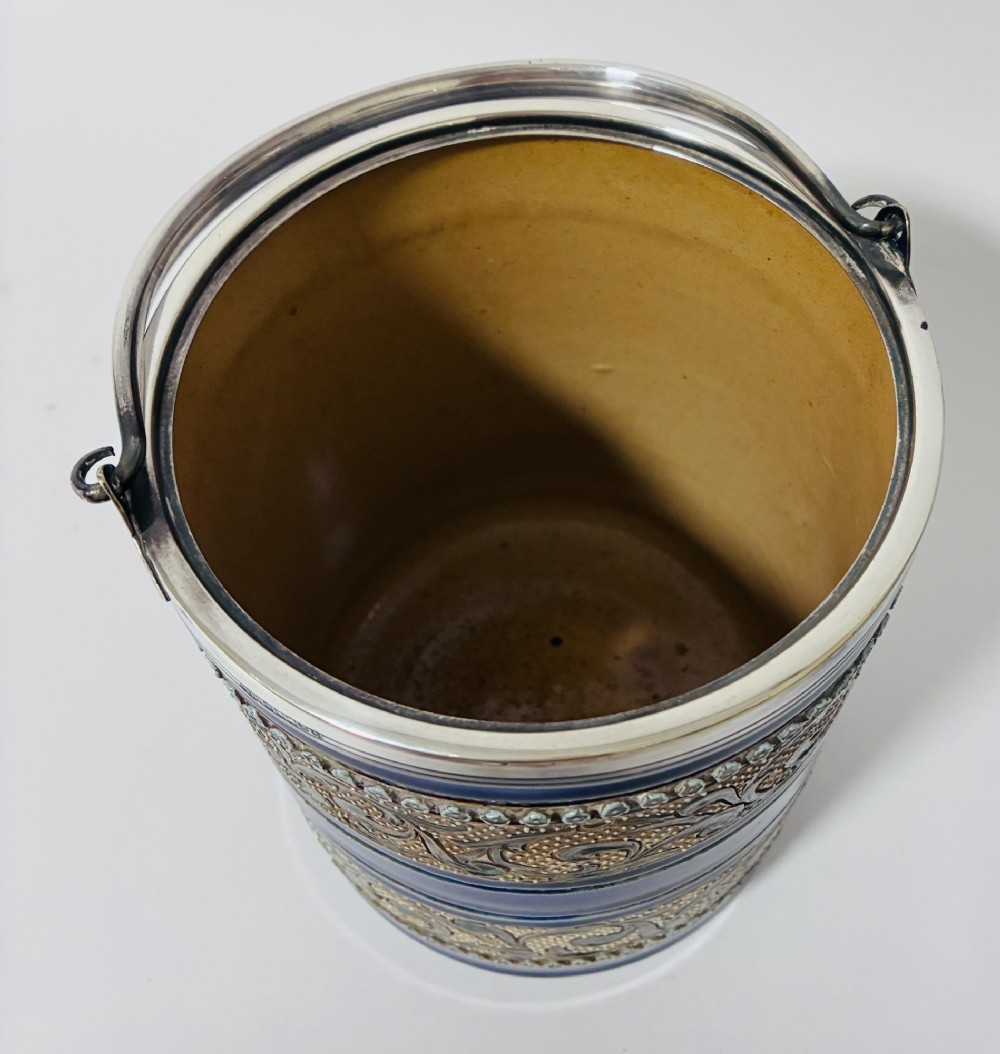 A cylindrical Victorian Doulton Lambeth stoneware biscuit barrel featuring cobalt blue and beige scrollwork decoration, fitted with a silver-plated lid, swing handle, and finial. View VI