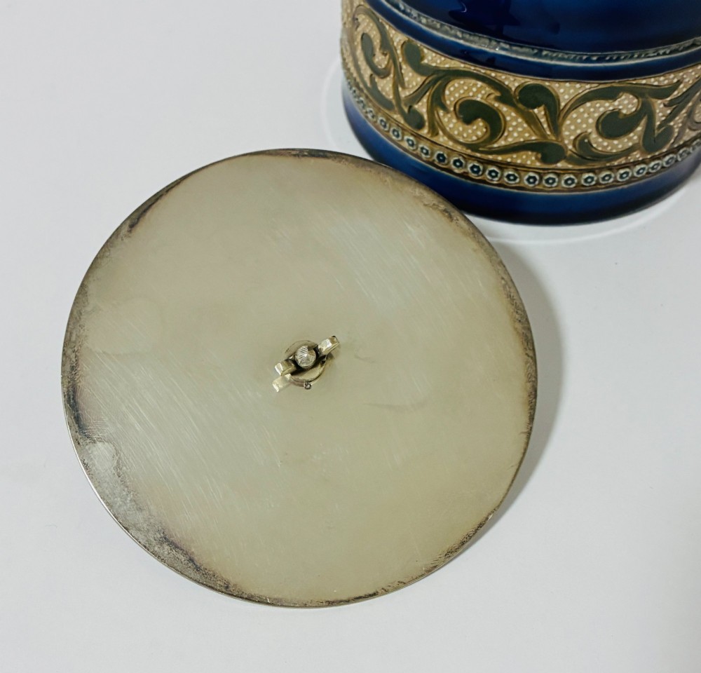 A cylindrical Victorian Doulton Lambeth stoneware biscuit barrel featuring cobalt blue and beige scrollwork decoration, fitted with a silver-plated lid, swing handle, and finial. View VII