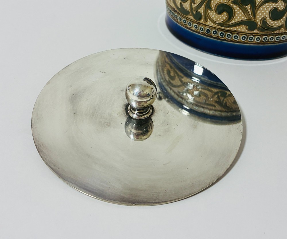 A cylindrical Victorian Doulton Lambeth stoneware biscuit barrel featuring cobalt blue and beige scrollwork decoration, fitted with a silver-plated lid, swing handle, and finial. View VIII