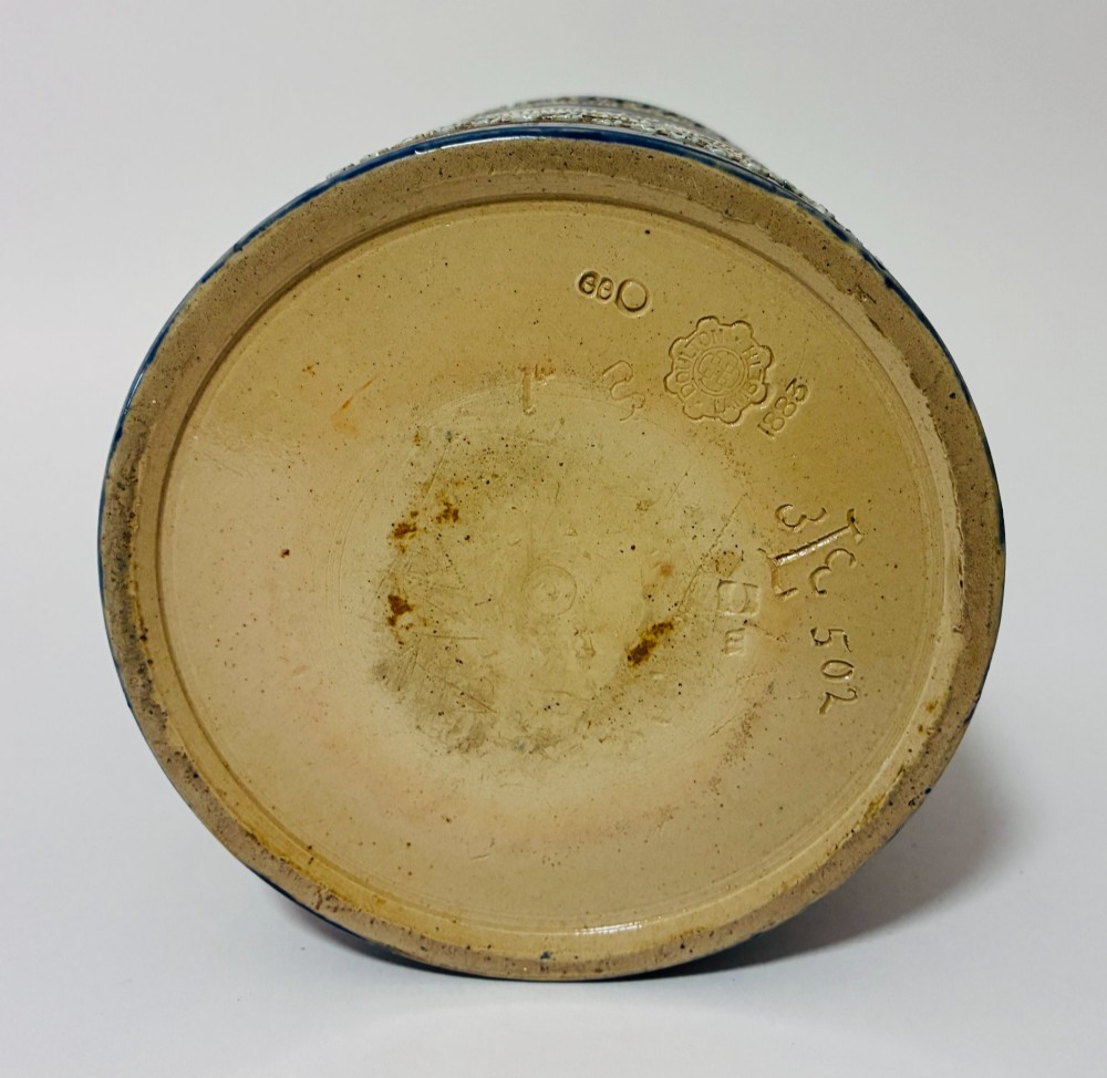 A cylindrical Victorian Doulton Lambeth stoneware biscuit barrel featuring cobalt blue and beige scrollwork decoration, fitted with a silver-plated lid, swing handle, and finial. View X