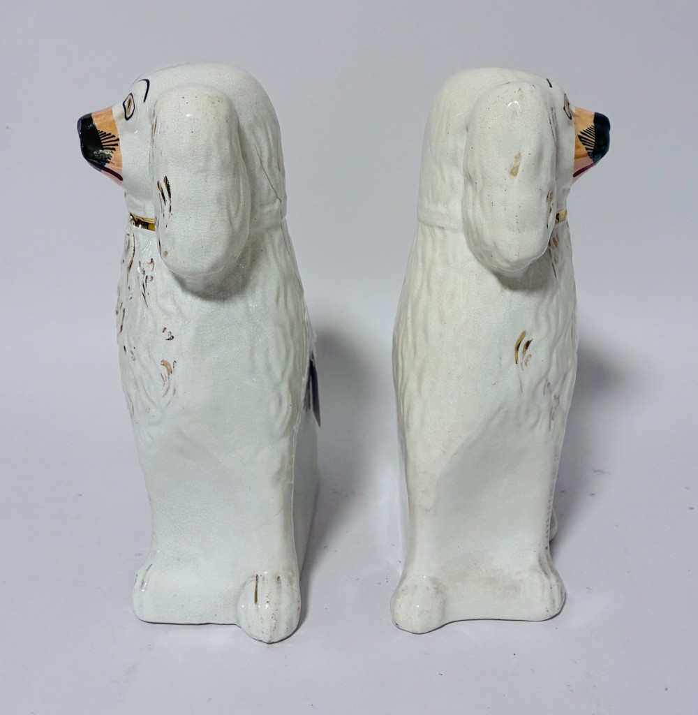 A pair of white glazed earthenware Staffordshire dog figures with hand-painted gold details and expressive facial features. View V