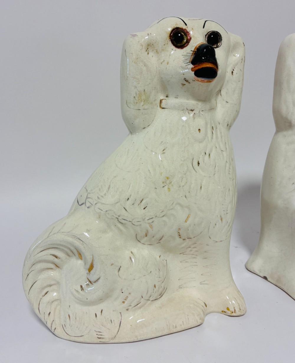 A pair of cream glazed ceramic Staffordshire spaniel figurines with black painted muzzles and amber eyes seated facing forward. View II