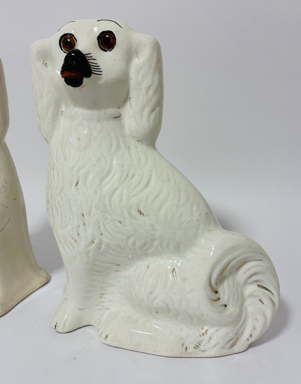 A pair of cream glazed ceramic Staffordshire spaniel figurines with black painted muzzles and amber eyes seated facing forward. View III