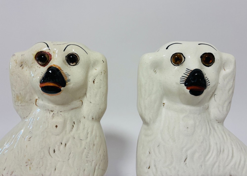 A pair of cream glazed ceramic Staffordshire spaniel figurines with black painted muzzles and amber eyes seated facing forward. View IV