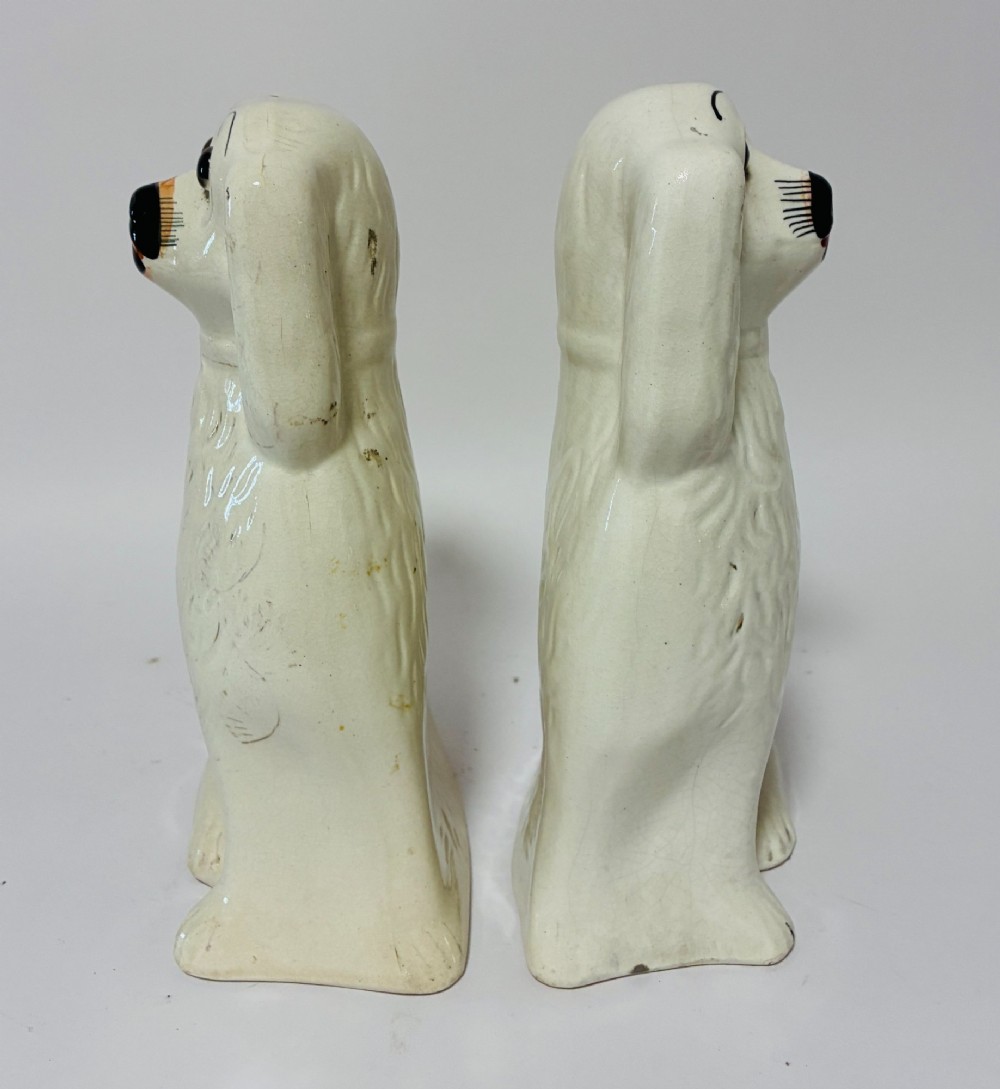 A pair of cream glazed ceramic Staffordshire spaniel figurines with black painted muzzles and amber eyes seated facing forward. View V