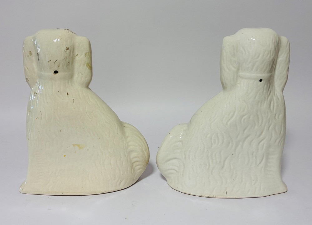 A pair of cream glazed ceramic Staffordshire spaniel figurines with black painted muzzles and amber eyes seated facing forward. View VI
