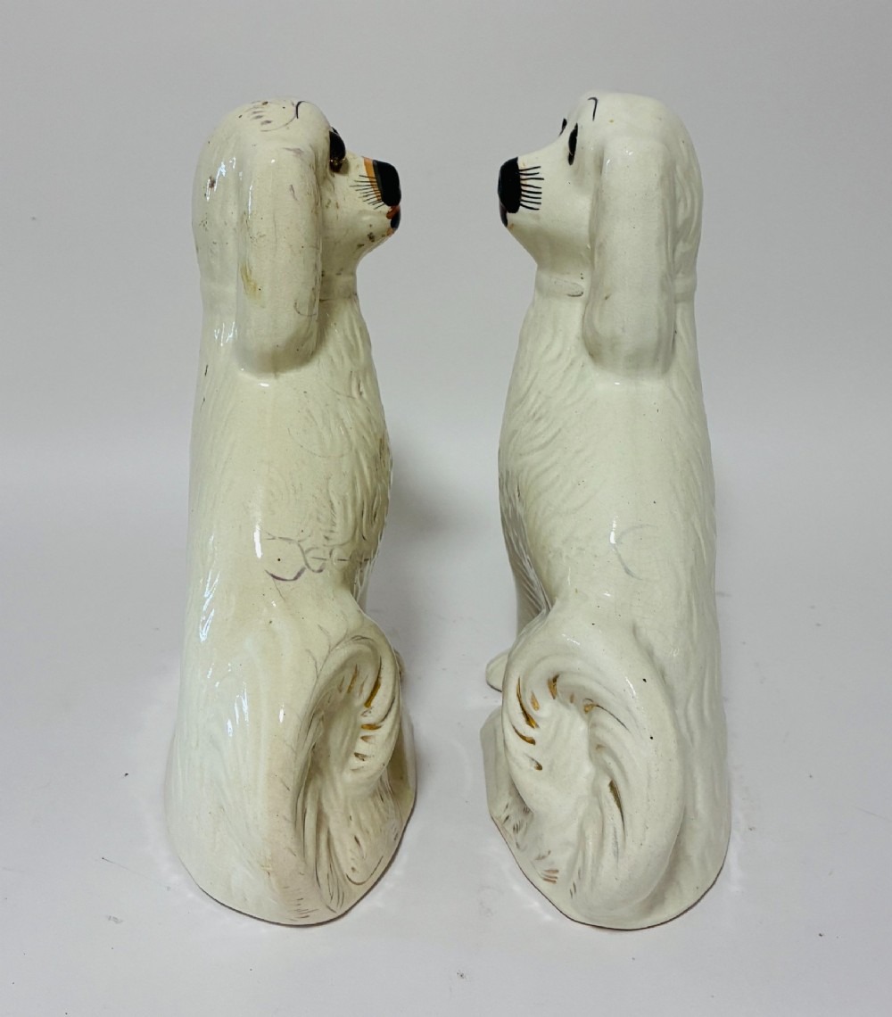 A pair of cream glazed ceramic Staffordshire spaniel figurines with black painted muzzles and amber eyes seated facing forward. View VII