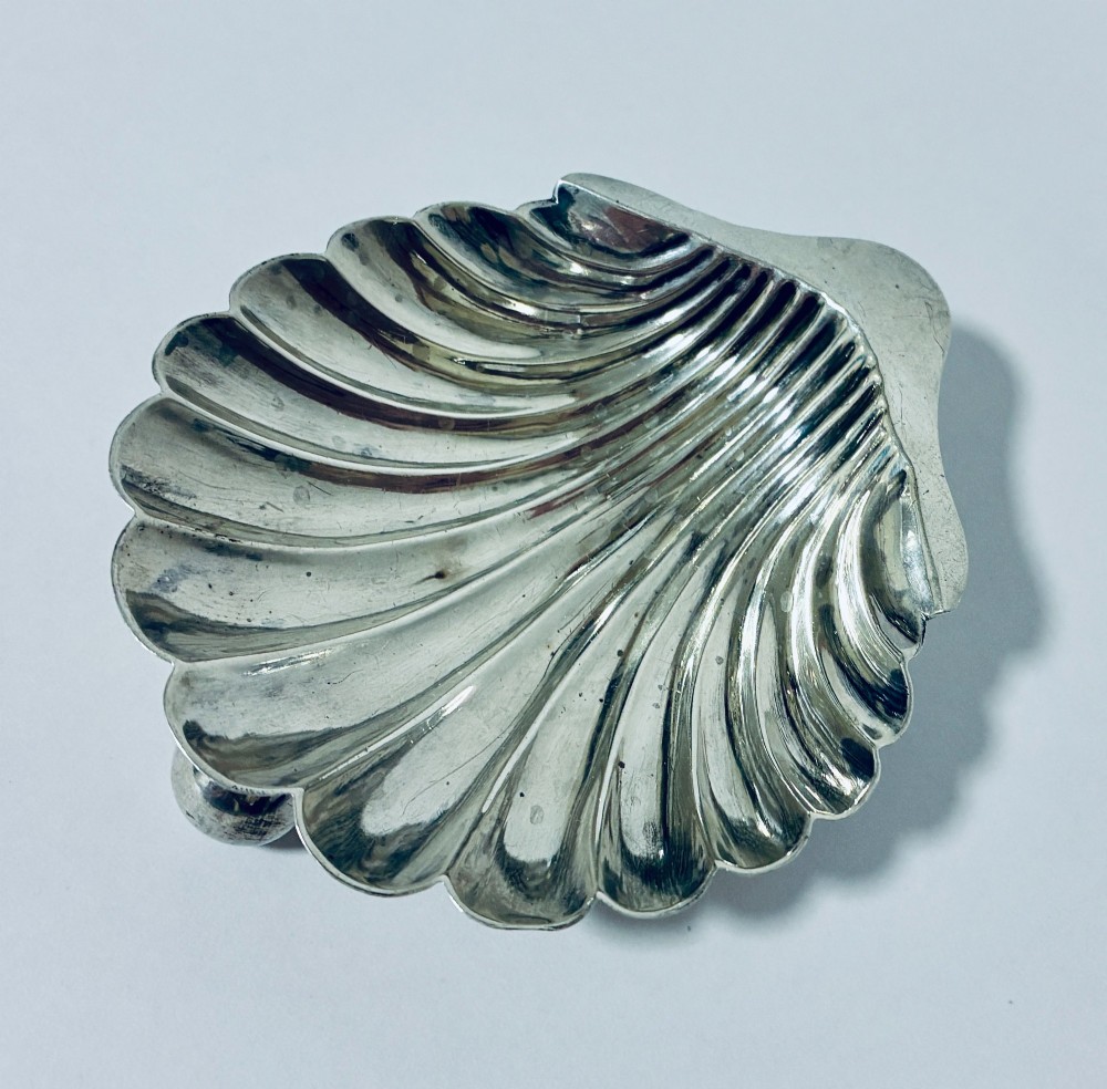 An antique silver-plated butter dish designed in the shape of a scalloped shell with fluted ridges and small ball feet.