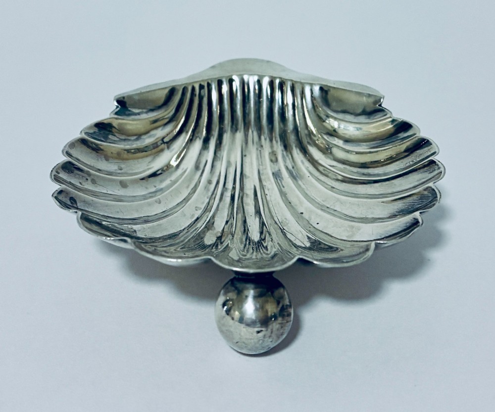An antique silver-plated butter dish designed in the shape of a scalloped shell with fluted ridges and small ball feet. View II