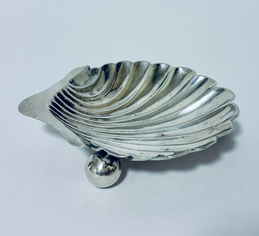 An antique silver-plated butter dish designed in the shape of a scalloped shell with fluted ridges and small ball feet. View V