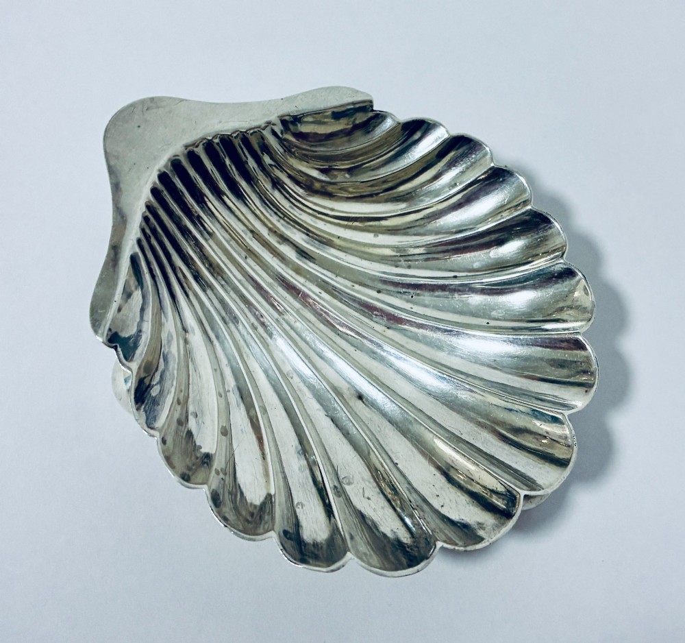 An antique silver-plated butter dish designed in the shape of a scalloped shell with fluted ridges and small ball feet. View VI