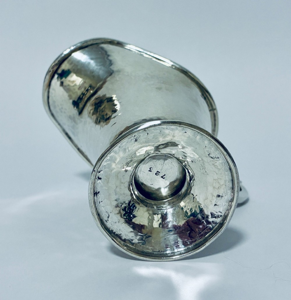 An antique sterling silver cream jug with a hand-hammered planished surface, a pedestal base, and an angular handle. View VIII