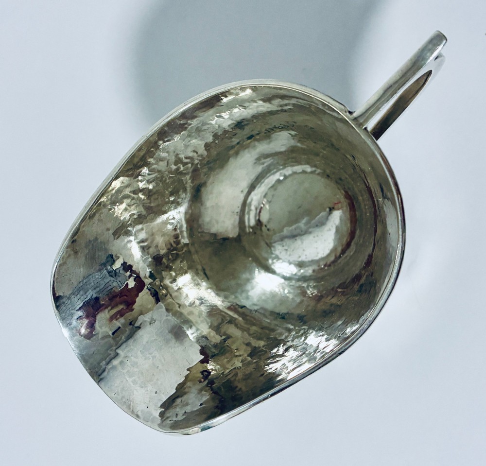 An antique sterling silver cream jug with a hand-hammered planished surface, a pedestal base, and an angular handle. View IX