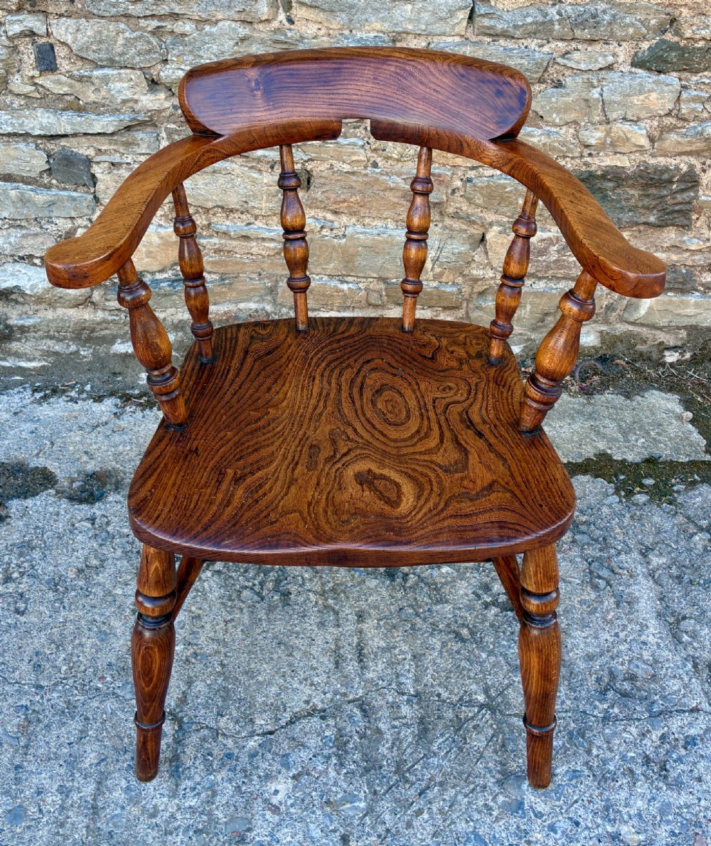 A Victorian elm captains armchair featuring a curved horseshoe rail, turned wooden spindles, and a deeply contoured saddle seat showing prominent wood grain.