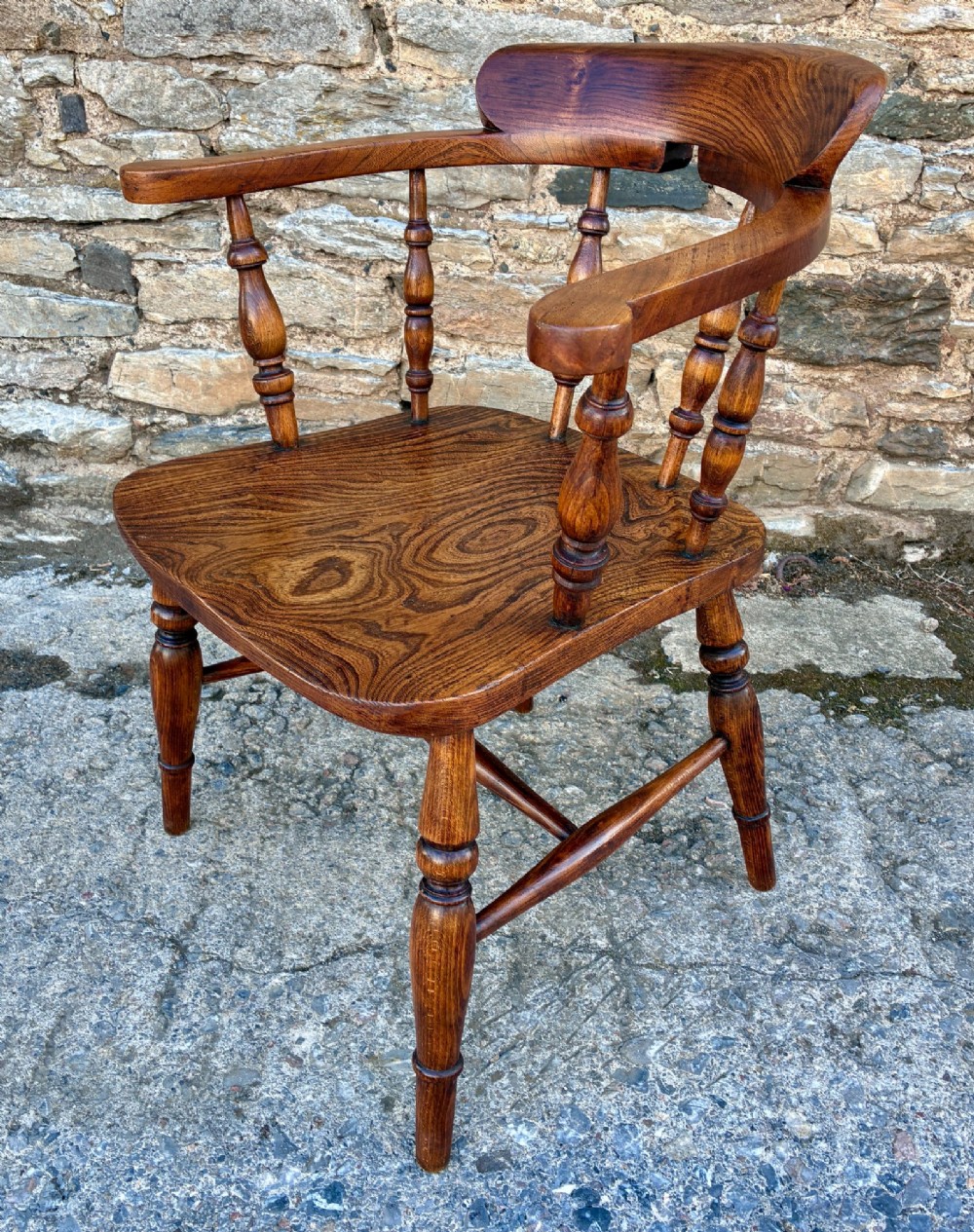 A Victorian elm captains armchair featuring a curved horseshoe rail, turned wooden spindles, and a deeply contoured saddle seat showing prominent wood grain. View V