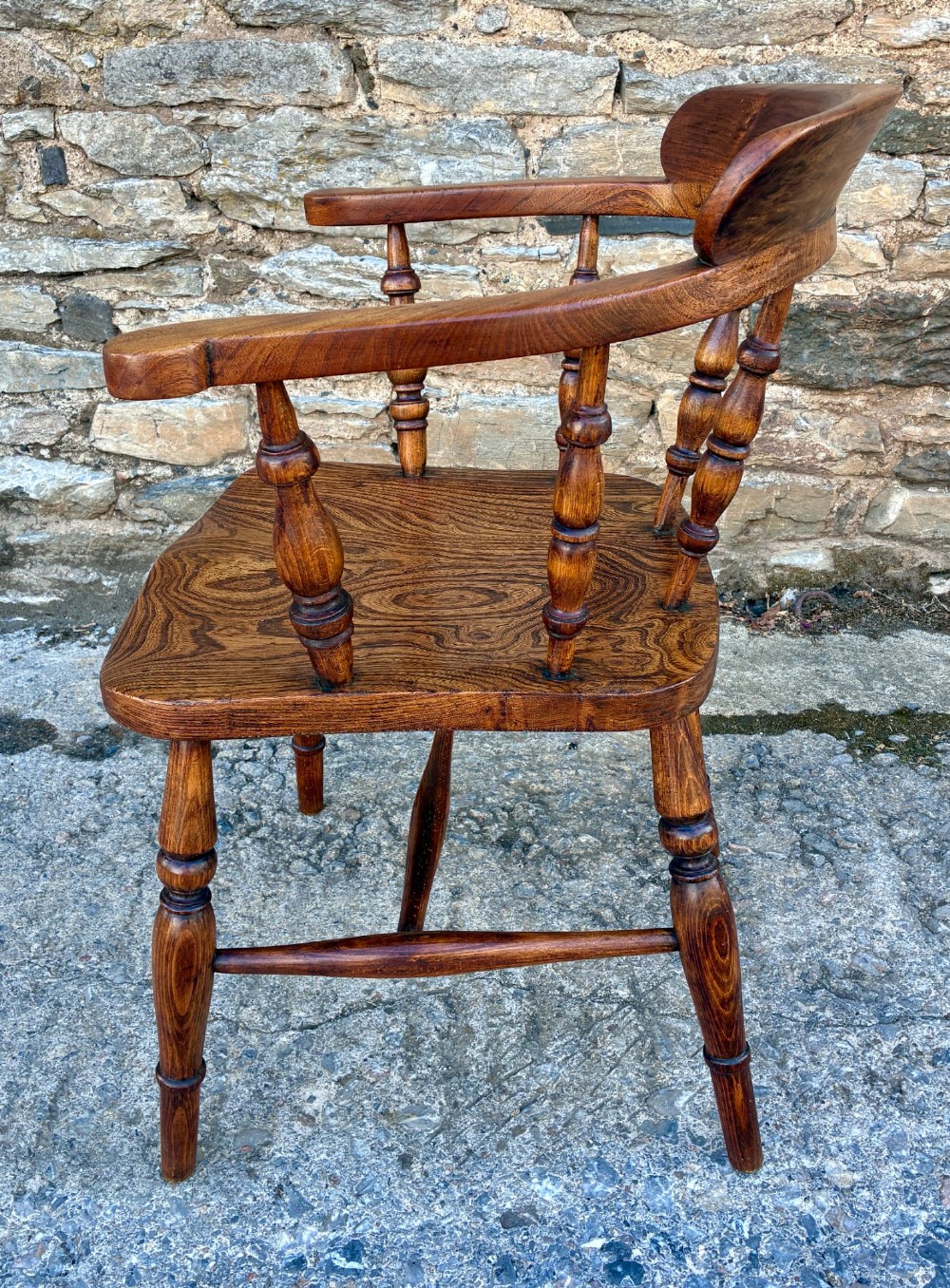 A Victorian elm captains armchair featuring a curved horseshoe rail, turned wooden spindles, and a deeply contoured saddle seat showing prominent wood grain. View VI