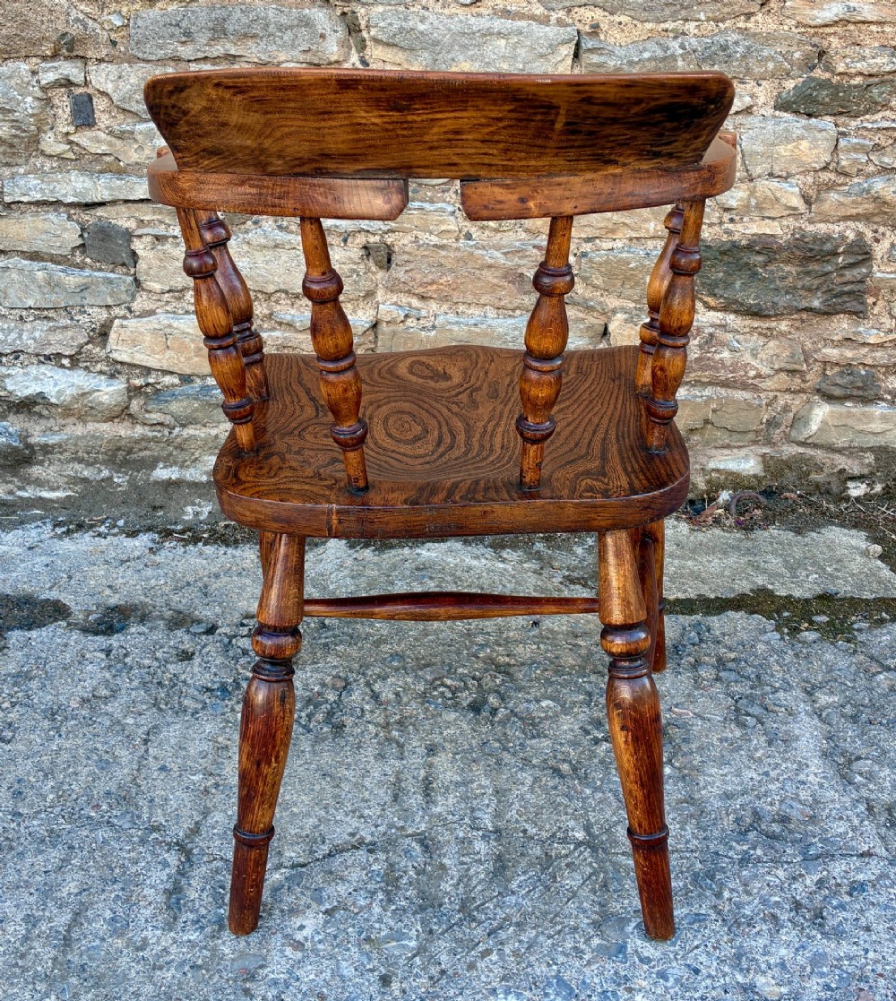 A Victorian elm captains armchair featuring a curved horseshoe rail, turned wooden spindles, and a deeply contoured saddle seat showing prominent wood grain. View VII