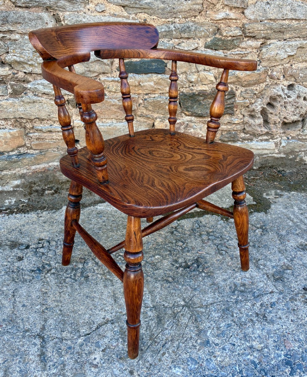 A Victorian elm captains armchair featuring a curved horseshoe rail, turned wooden spindles, and a deeply contoured saddle seat showing prominent wood grain. View X