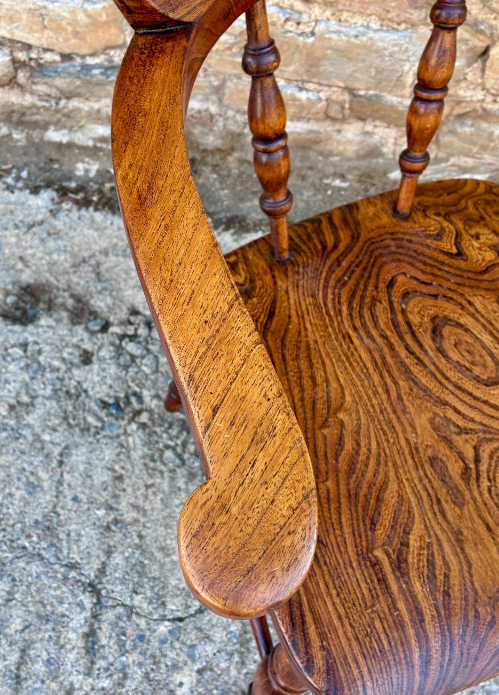 A Victorian elm captains armchair featuring a curved horseshoe rail, turned wooden spindles, and a deeply contoured saddle seat showing prominent wood grain. View XI