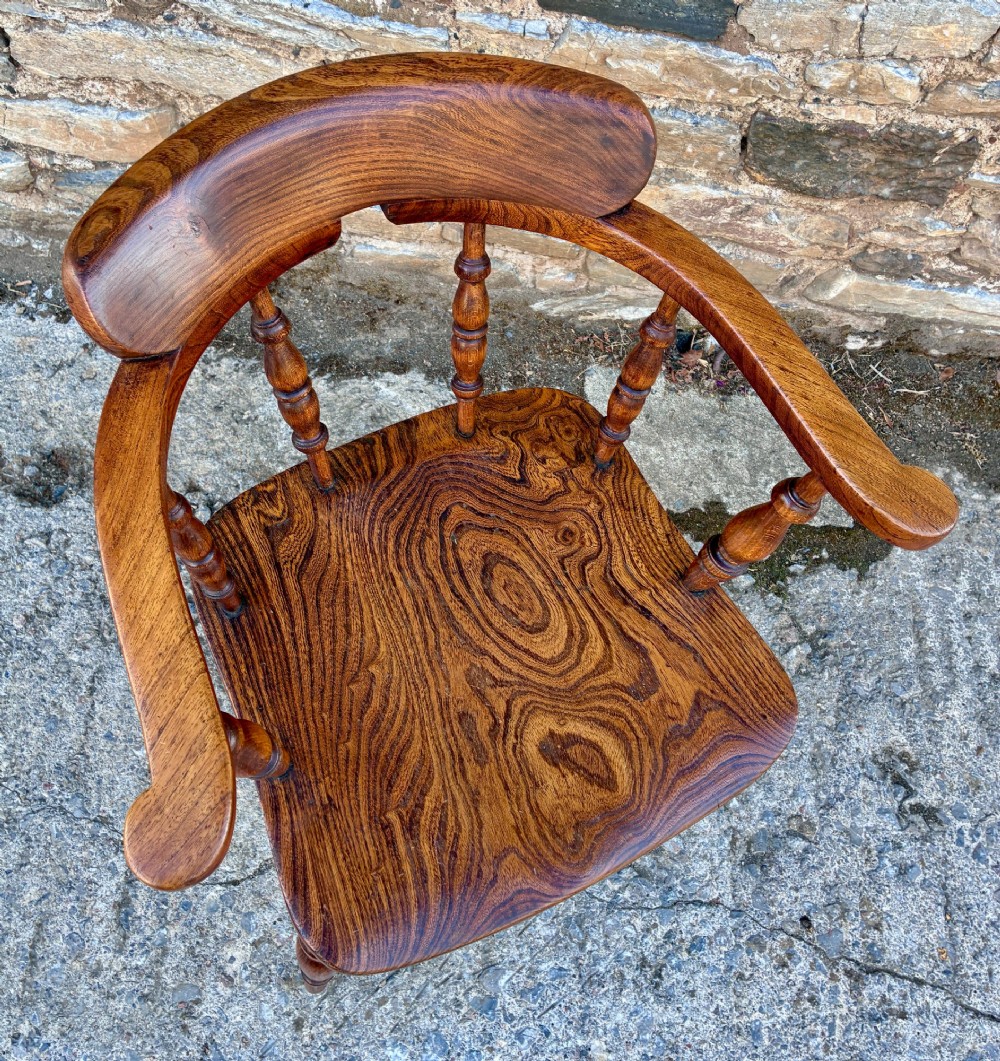 A Victorian elm captains armchair featuring a curved horseshoe rail, turned wooden spindles, and a deeply contoured saddle seat showing prominent wood grain. View XII