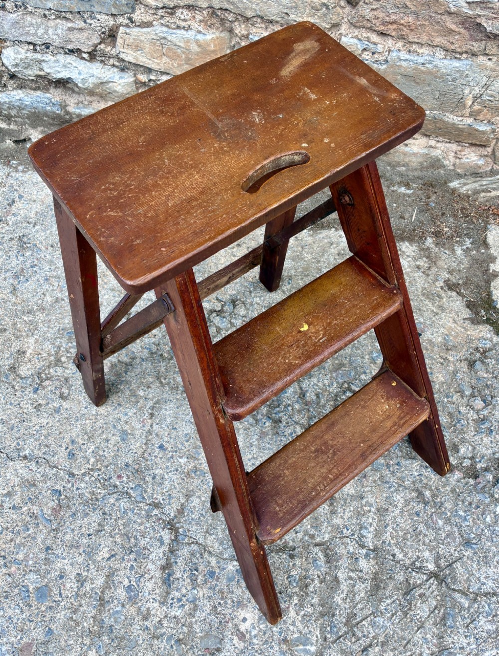 A vintage wooden folding step stool with three tread steps and metal side bracing finished in a warm reddish-brown stain. View II