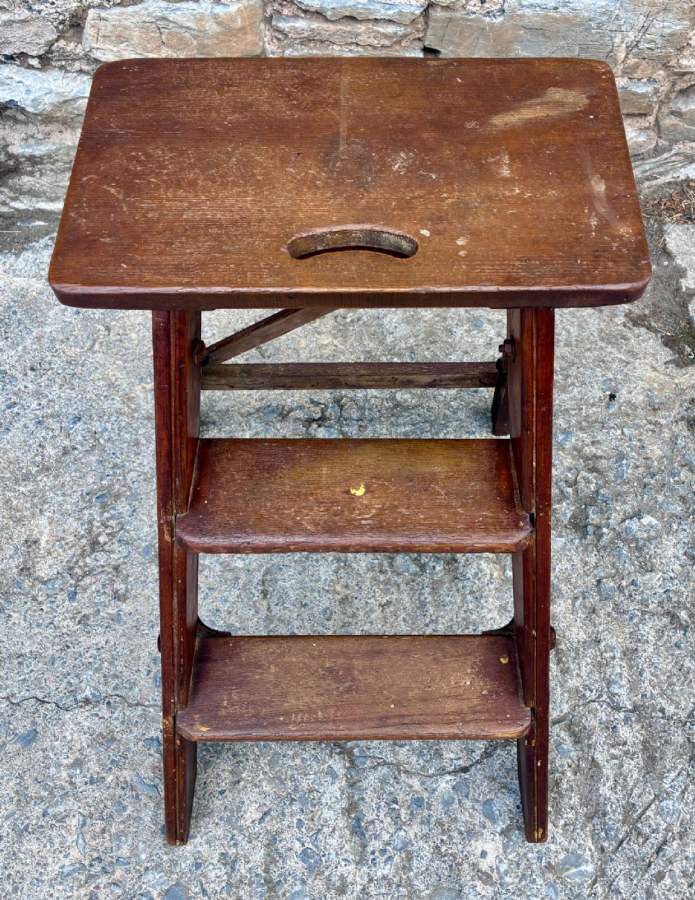 A vintage wooden folding step stool with three tread steps and metal side bracing finished in a warm reddish-brown stain. View III