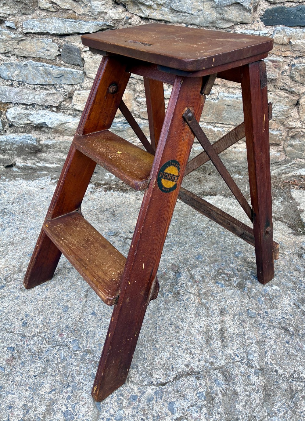 A vintage wooden folding step stool with three tread steps and metal side bracing finished in a warm reddish-brown stain. View IV
