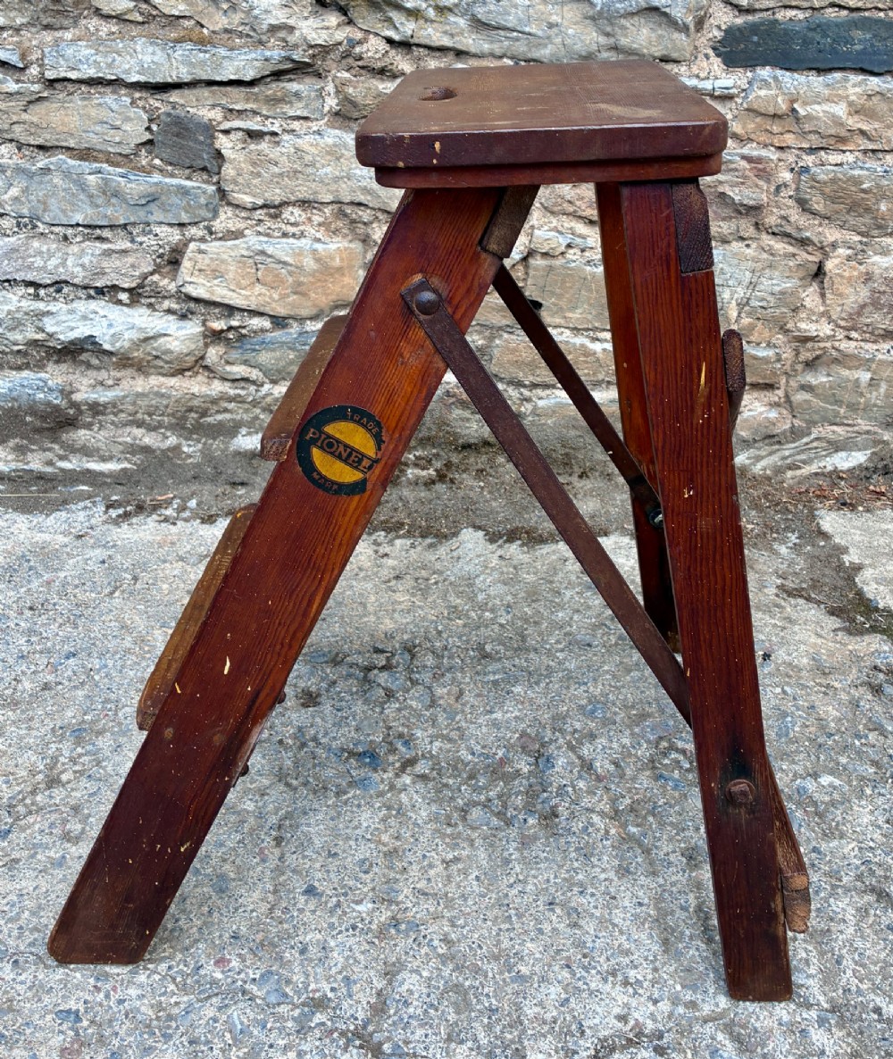 A vintage wooden folding step stool with three tread steps and metal side bracing finished in a warm reddish-brown stain. View VI