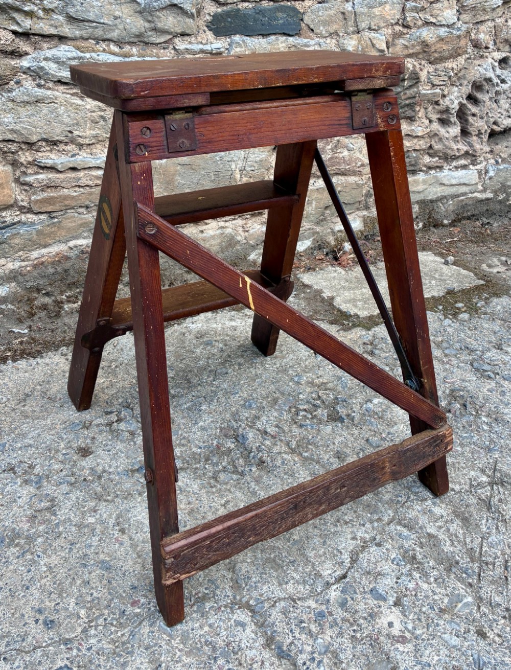 A vintage wooden folding step stool with three tread steps and metal side bracing finished in a warm reddish-brown stain. View VIII