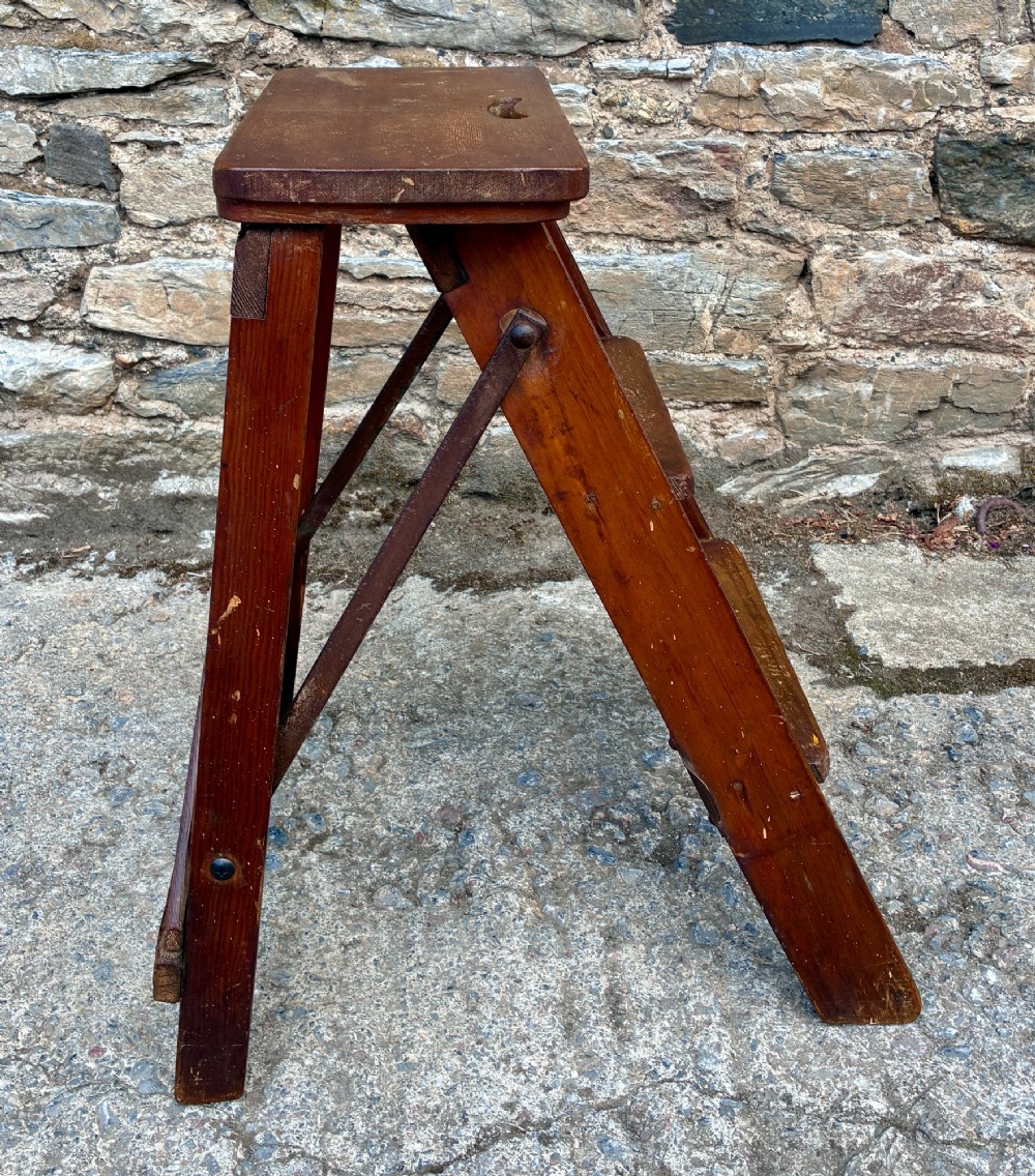A vintage wooden folding step stool with three tread steps and metal side bracing finished in a warm reddish-brown stain. View IX
