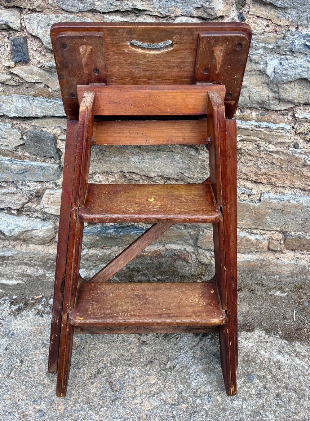 A vintage wooden folding step stool with three tread steps and metal side bracing finished in a warm reddish-brown stain. View X