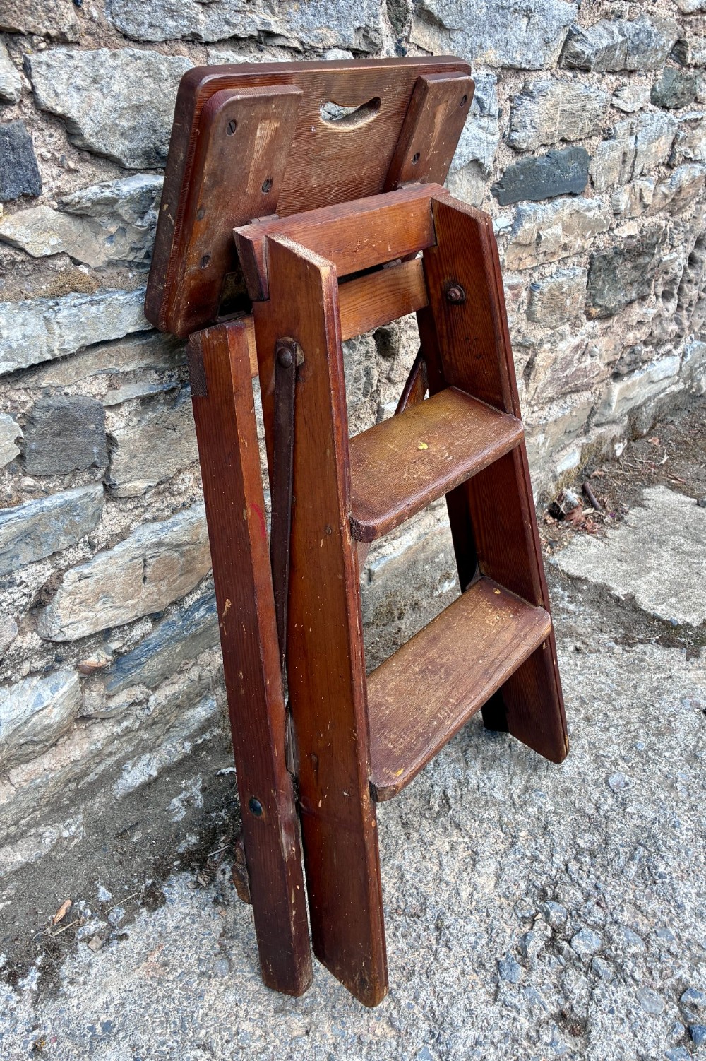 A vintage wooden folding step stool with three tread steps and metal side bracing finished in a warm reddish-brown stain. View XI