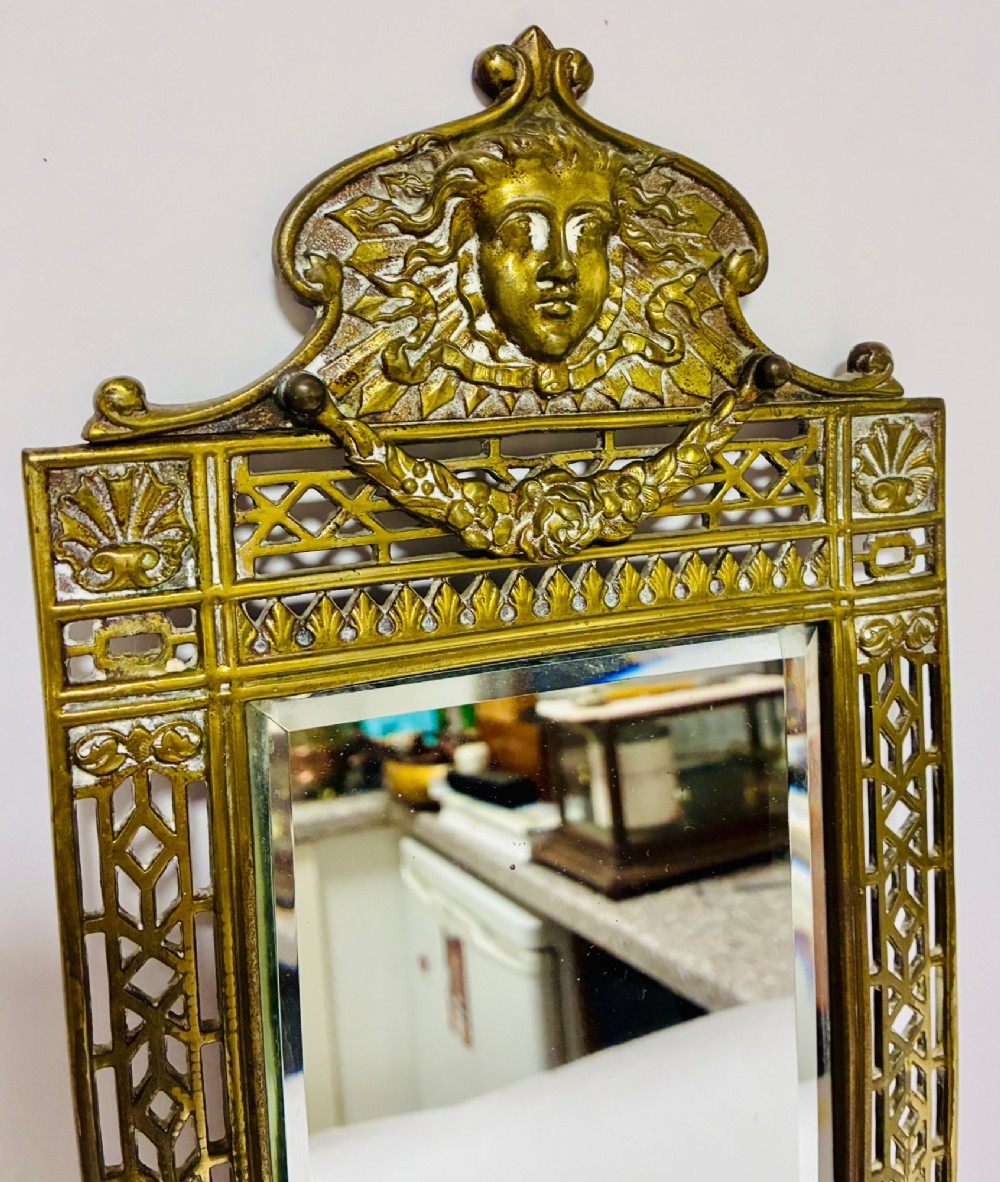 An ornate cast brass wall mirror featuring a central bevelled glass plate, openwork lattice frame, top mask cresting, and an integrated lower tray. View III