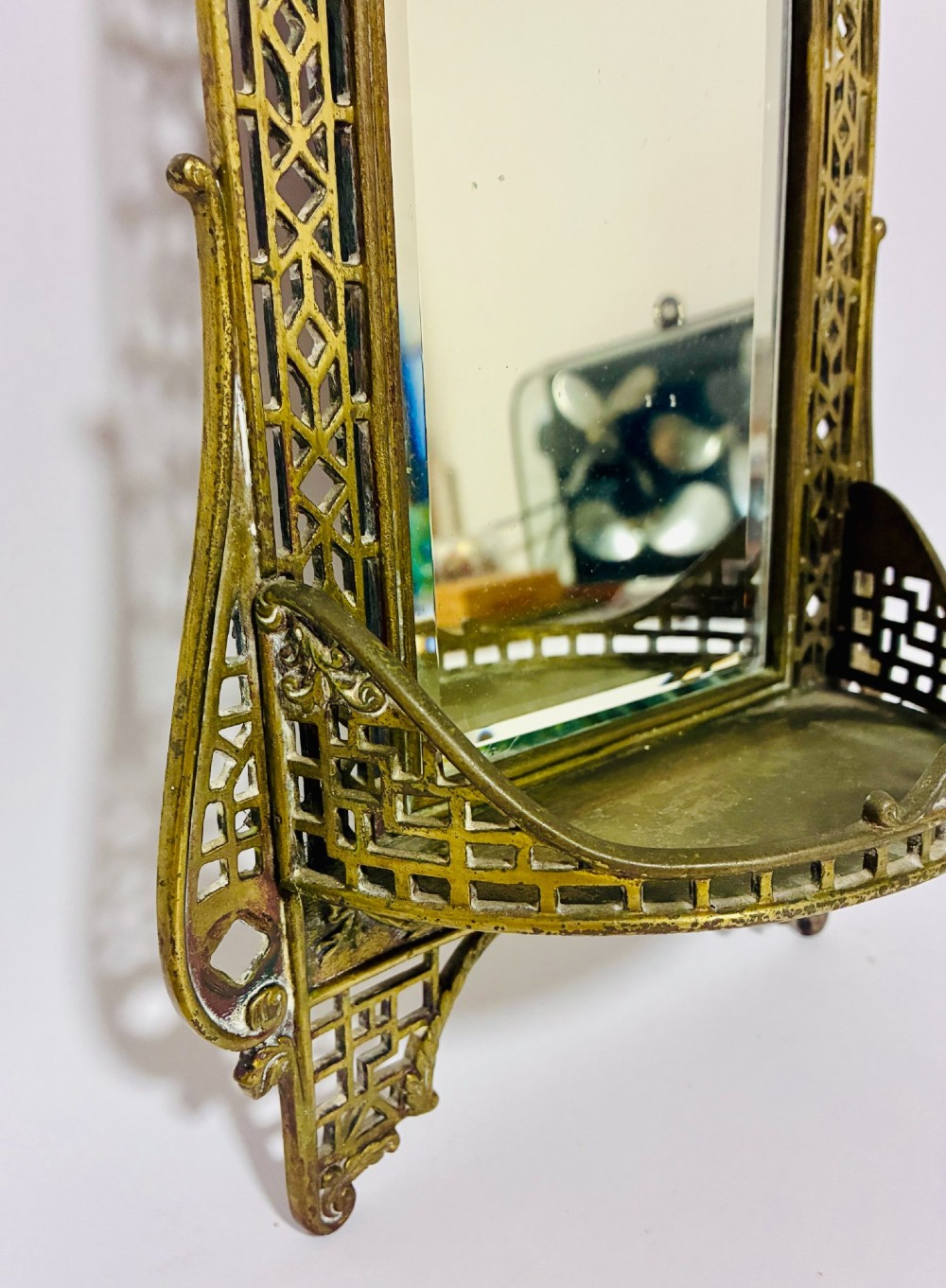 An ornate cast brass wall mirror featuring a central bevelled glass plate, openwork lattice frame, top mask cresting, and an integrated lower tray. View IV