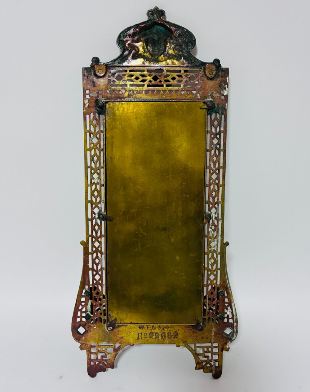 An ornate cast brass wall mirror featuring a central bevelled glass plate, openwork lattice frame, top mask cresting, and an integrated lower tray. View VII