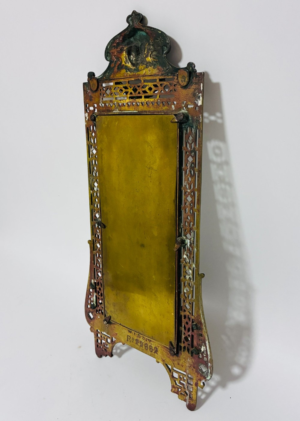 An ornate cast brass wall mirror featuring a central bevelled glass plate, openwork lattice frame, top mask cresting, and an integrated lower tray. View IX