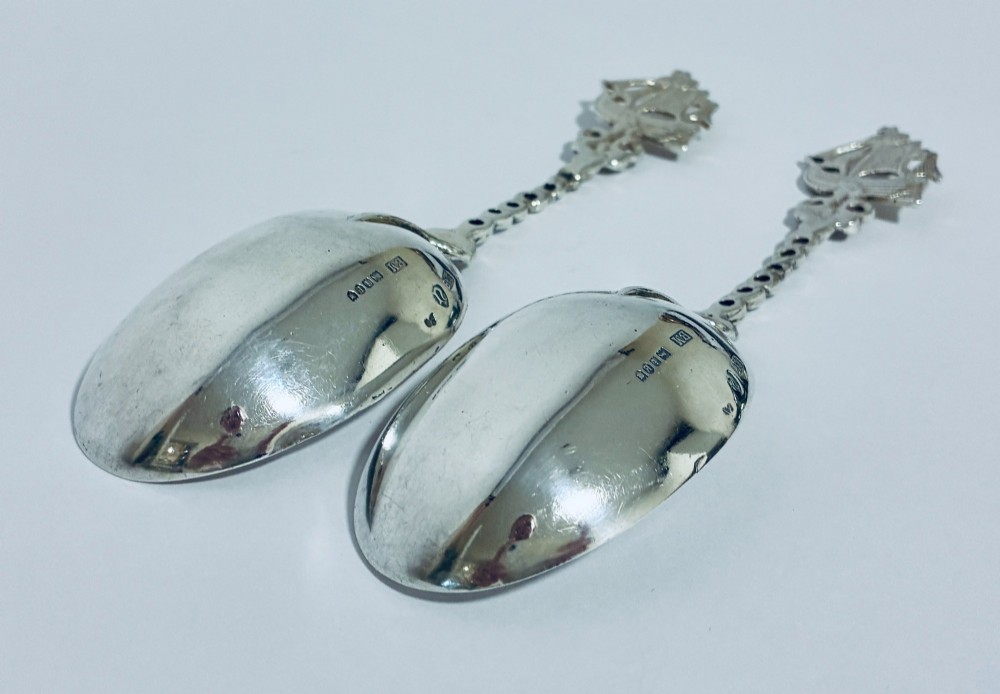 A pair of antique silver spoons featuring oval bowls, decorative spiral stems, and detailed sailing ship finials displayed against a plain background. View V