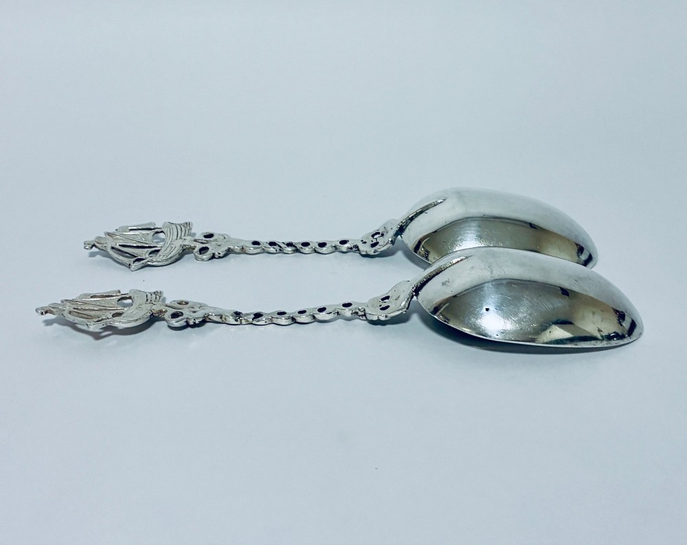A pair of antique silver spoons featuring oval bowls, decorative spiral stems, and detailed sailing ship finials displayed against a plain background. View VI