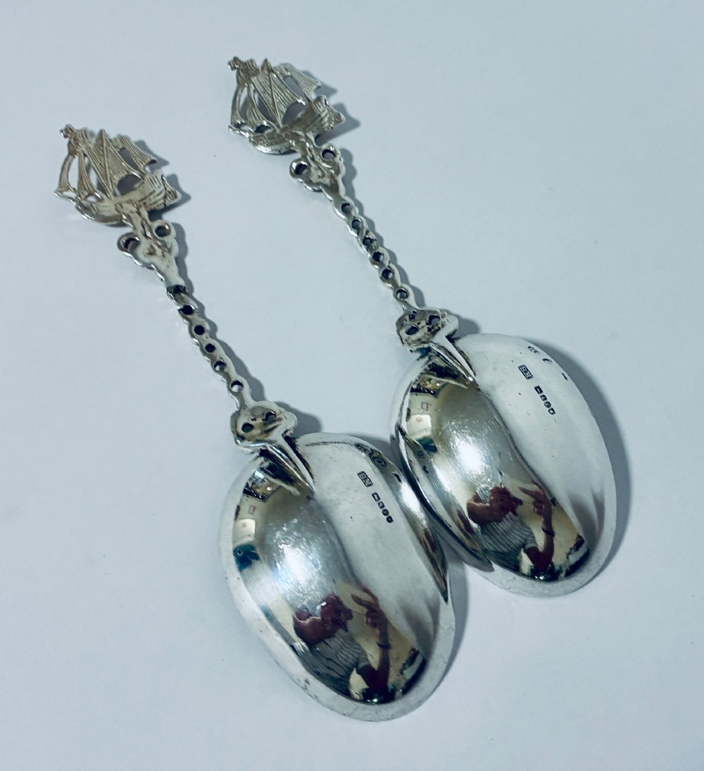 A pair of antique silver spoons featuring oval bowls, decorative spiral stems, and detailed sailing ship finials displayed against a plain background. View VII