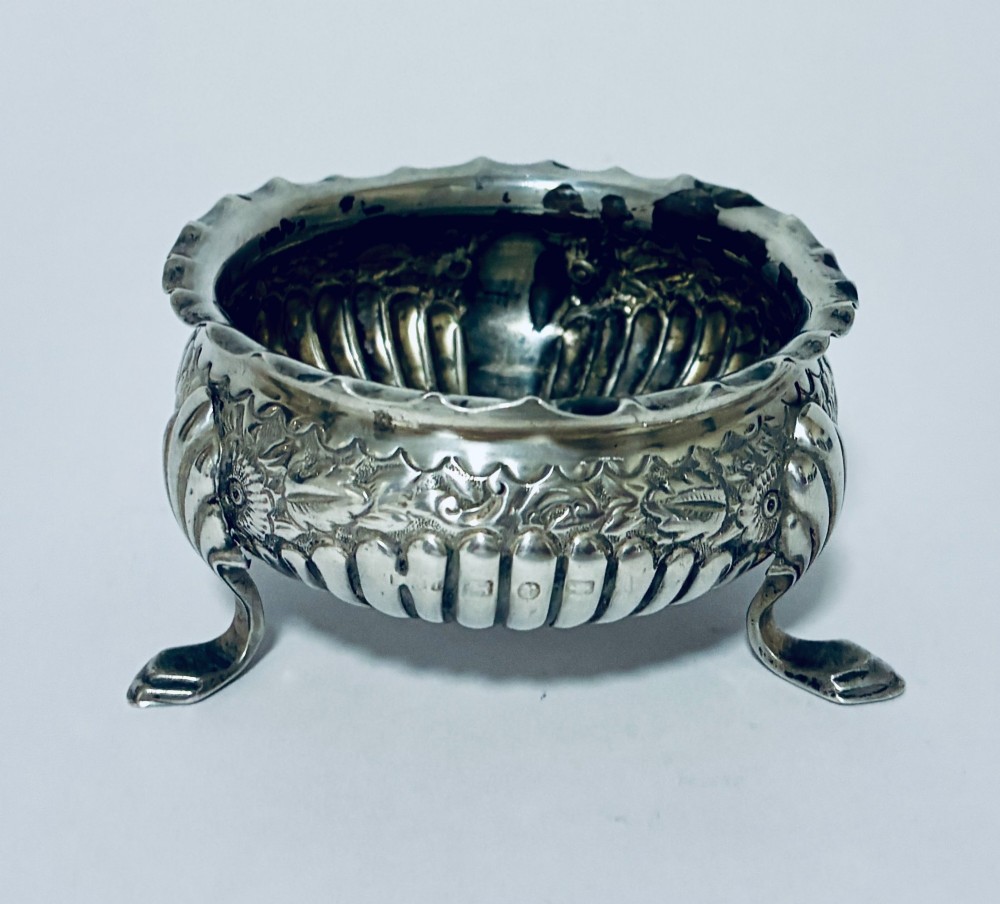 A small Victorian sterling silver salt dish with a crimped rim, chased floral decoration, fluted lower body, and three tripod legs. View III