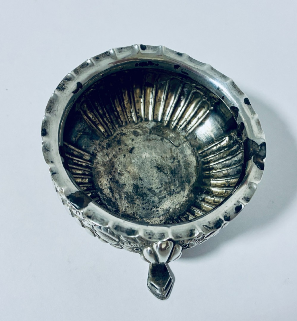 A small Victorian sterling silver salt dish with a crimped rim, chased floral decoration, fluted lower body, and three tripod legs. View IV