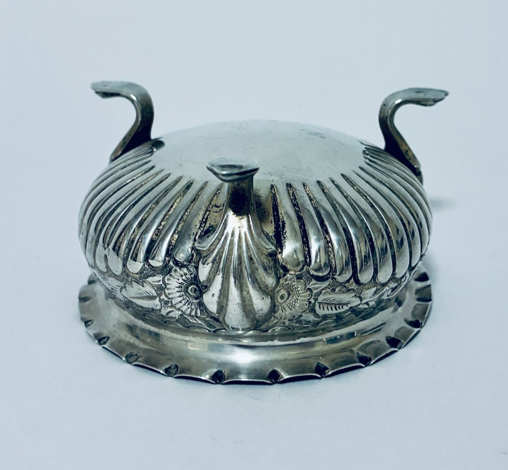 A small Victorian sterling silver salt dish with a crimped rim, chased floral decoration, fluted lower body, and three tripod legs. View V