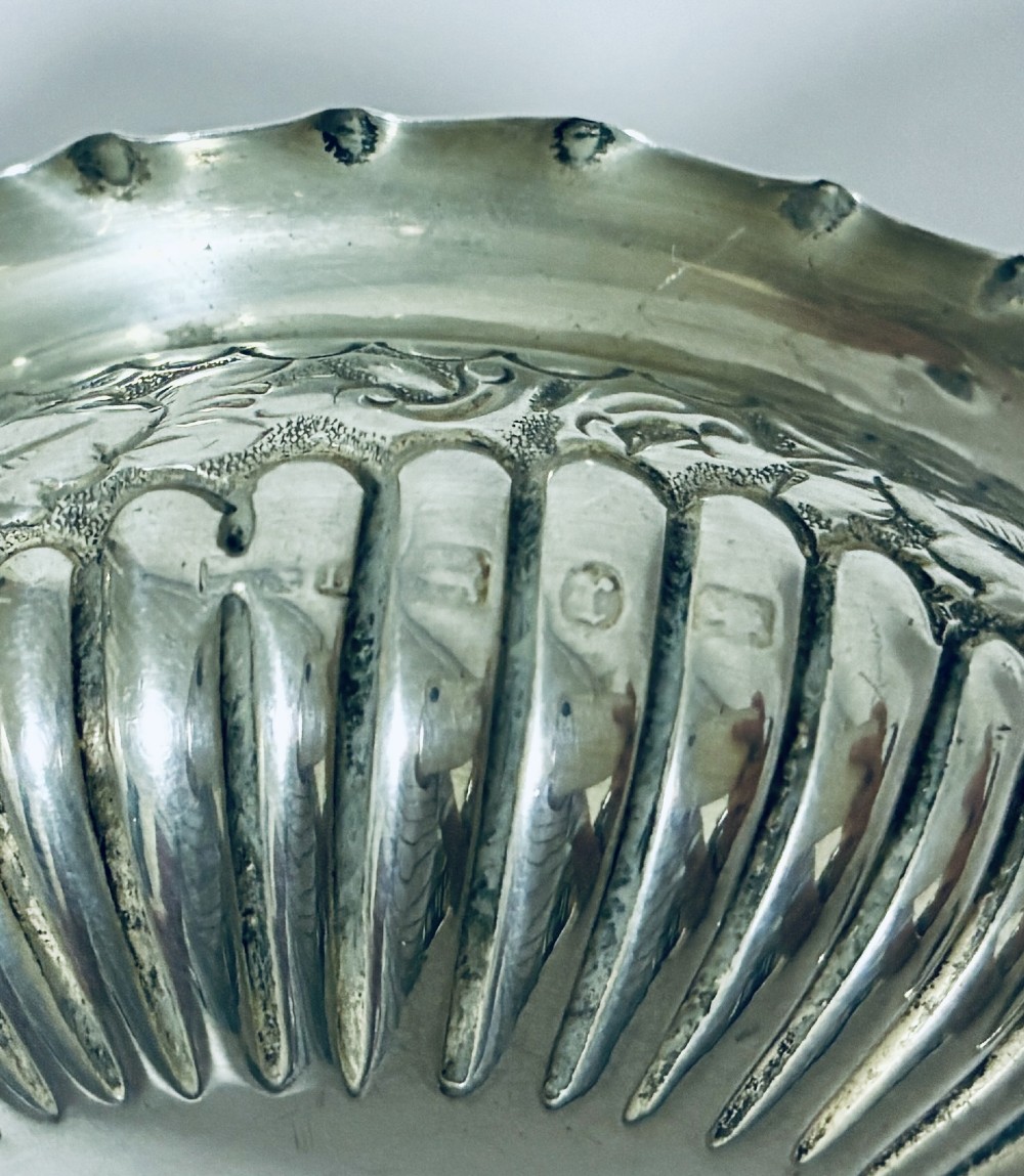 A small Victorian sterling silver salt dish with a crimped rim, chased floral decoration, fluted lower body, and three tripod legs. View VII