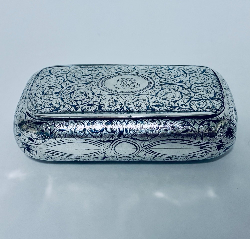A small, rectangular silver snuff box with rounded corners featuring intricate hand-engraved scrollwork patterns and a central oval cartouche.